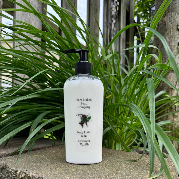 A pump bottle of Bare Naked body lotion with Lavender & Vanilla scents, placed on a stone surface with green plants in the background.
