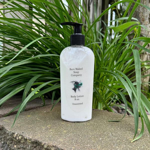 A pump bottle of unscented body lotion labeled 'Bare Naked' placed on a stone surface with green plants in the background.