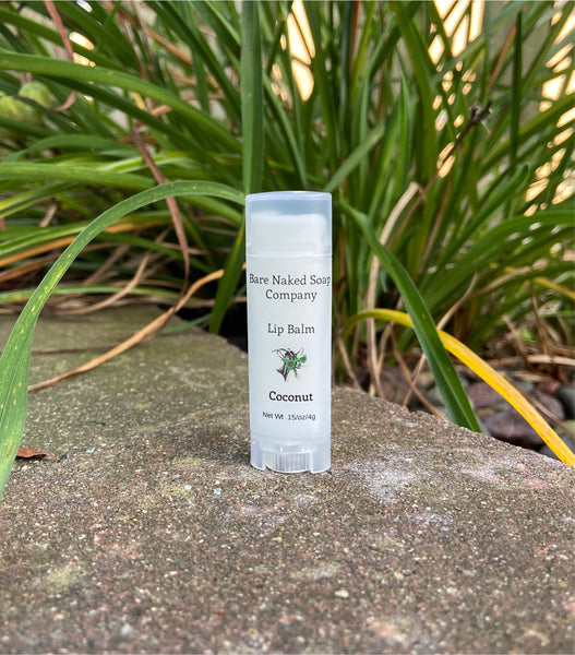A tube of lip balm with coconut flavor placed on a stone surface with grass in the background.