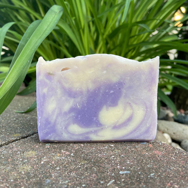 purple and white swirls in this luxury lavender soap sitting on a rock outside with foliage in the background