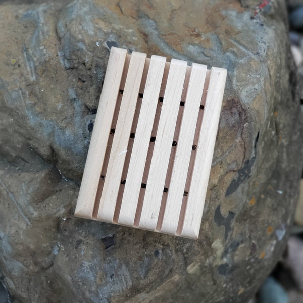A wooden draining soap dish placed on a rock surface.